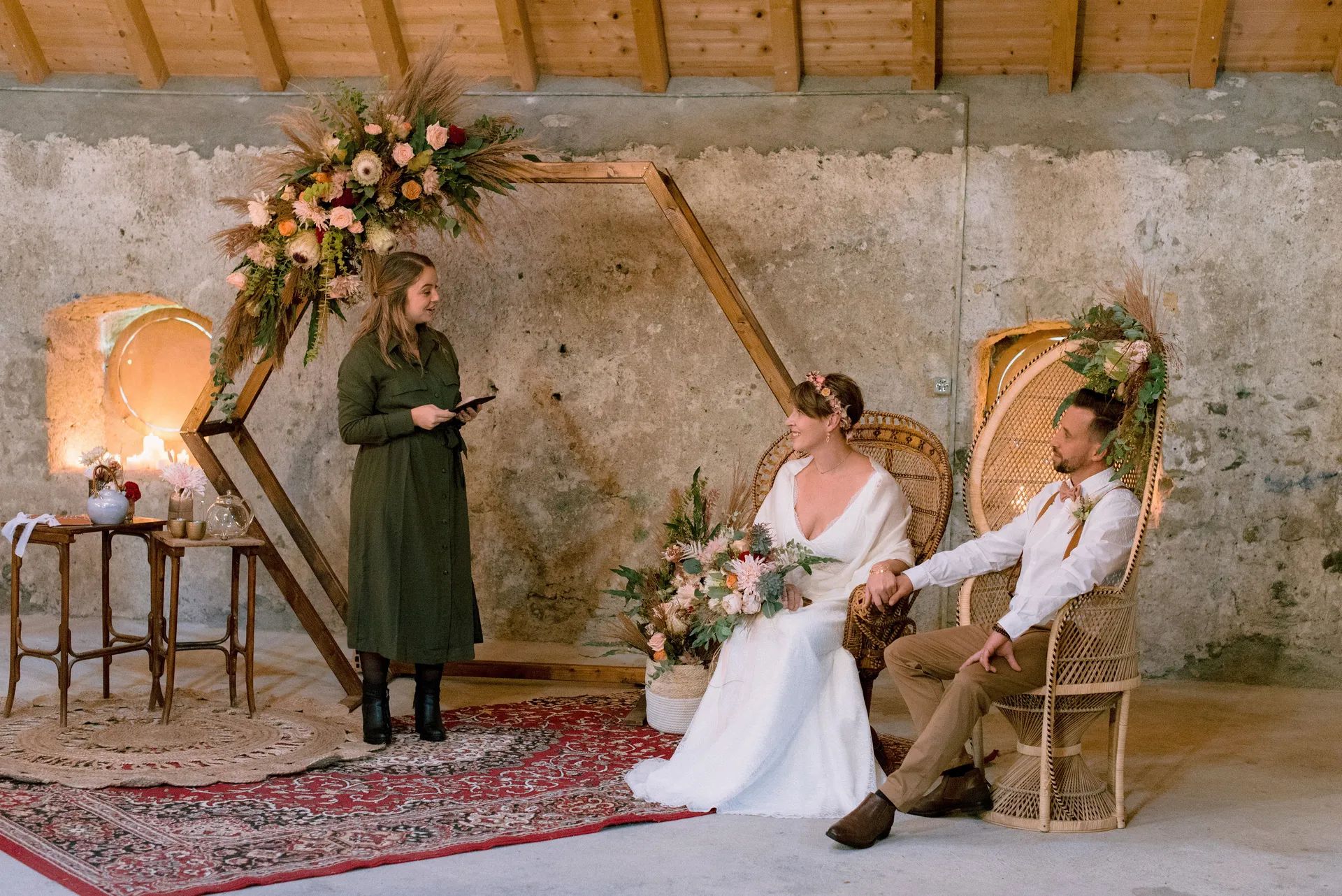 Cérémonie dans une grange : mariés assis, officiante et arche fleurie