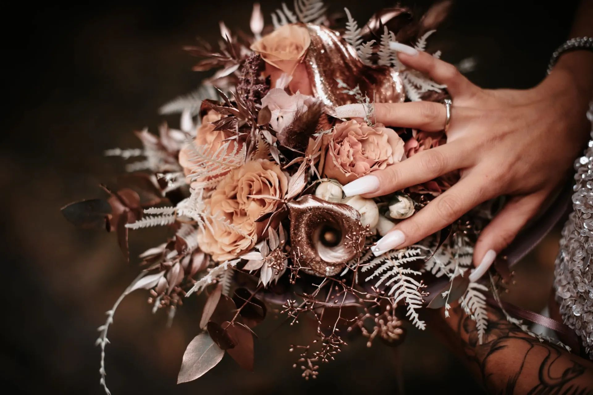 Main de la mariée tenant un bouquet de roses cuivrées et de fleurs séchées