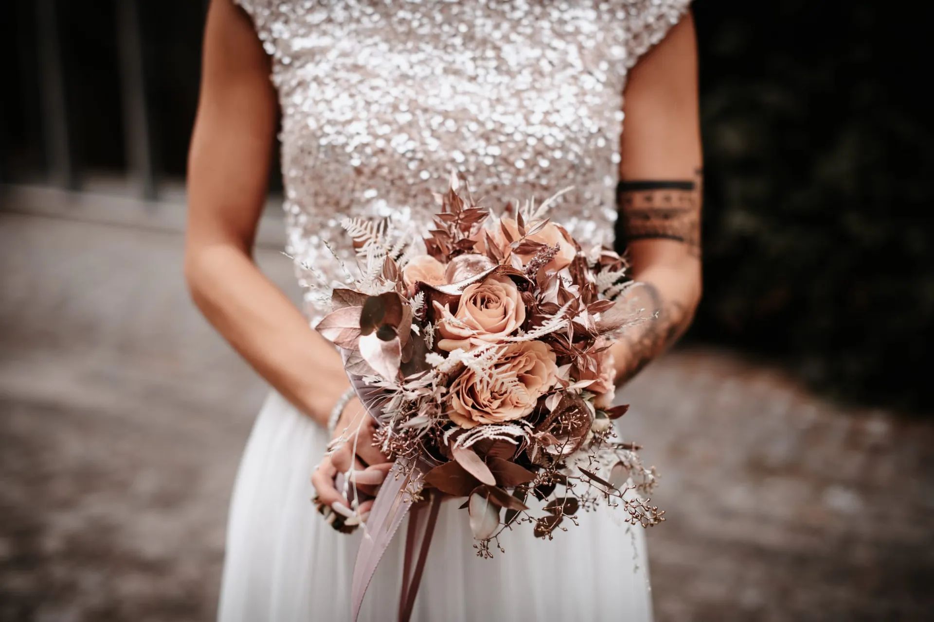 Mariée en haut à sequins tenant un bouquet de roses cuivrées