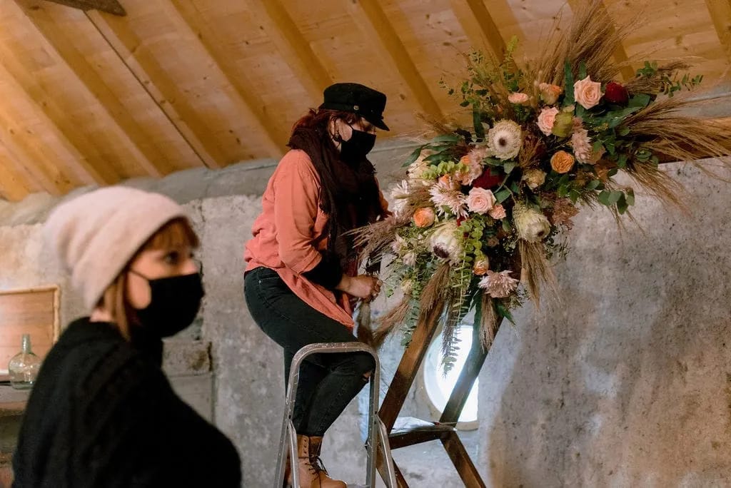 Installation de l’arche fleurie sur un escabeau, dans une grange
