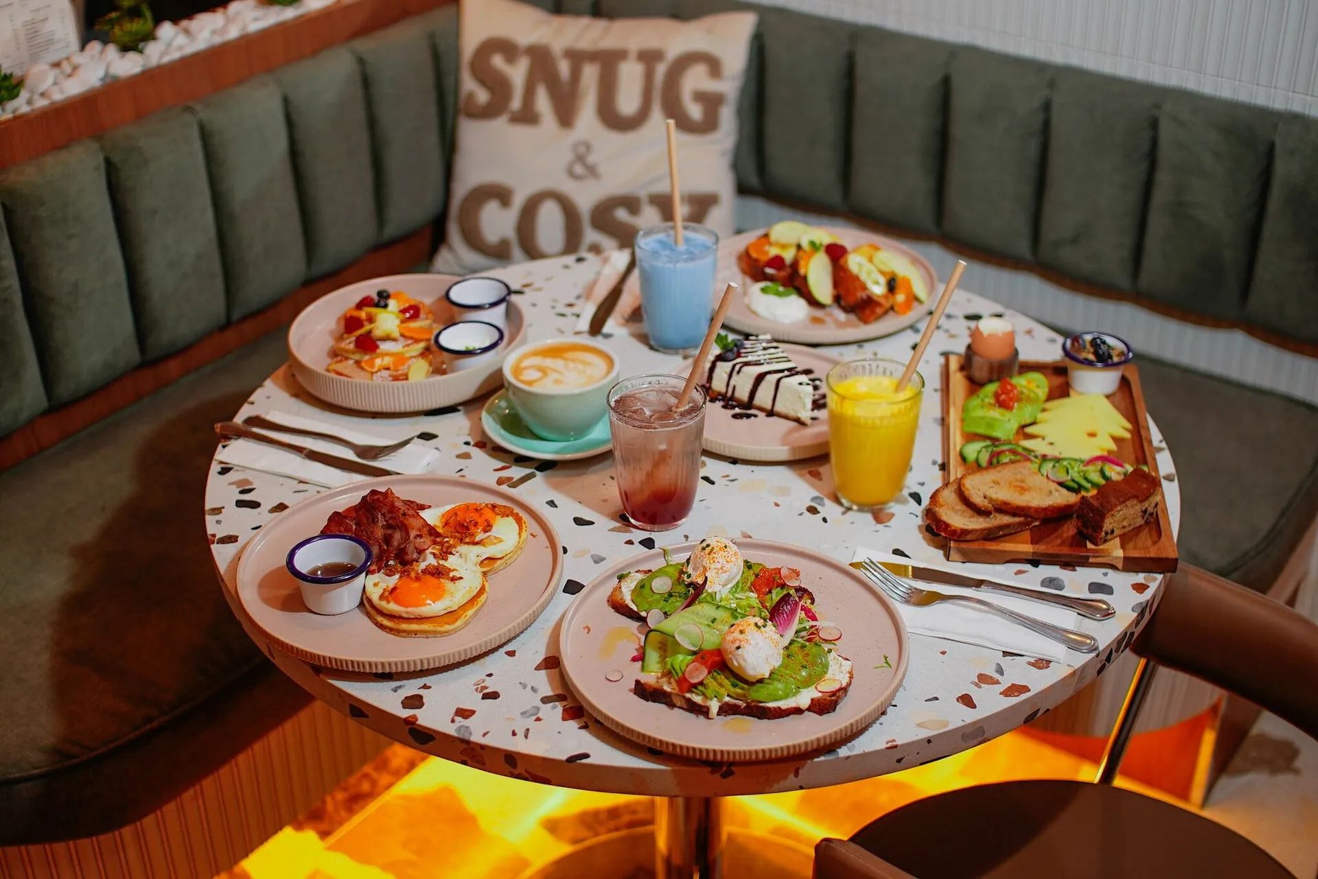 Une table de brunch dressée devant la banquette sauge et le coussin Snug & Cosy