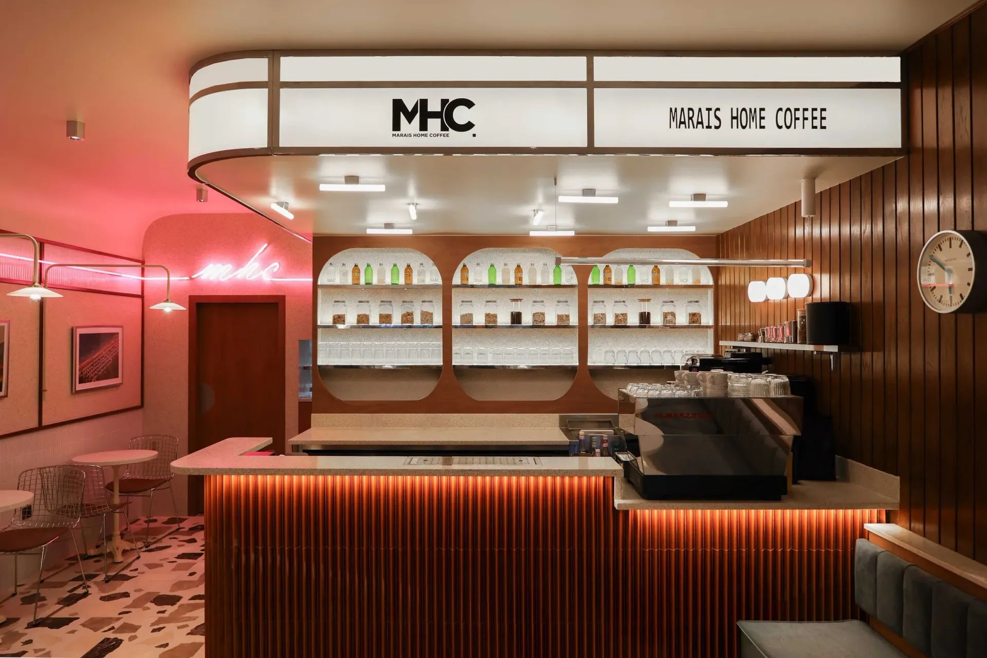La salle de Marais Home Coffee : le comptoir sous l'enseigne MHC, les chaises en fil blanc et le sol en terrazzo