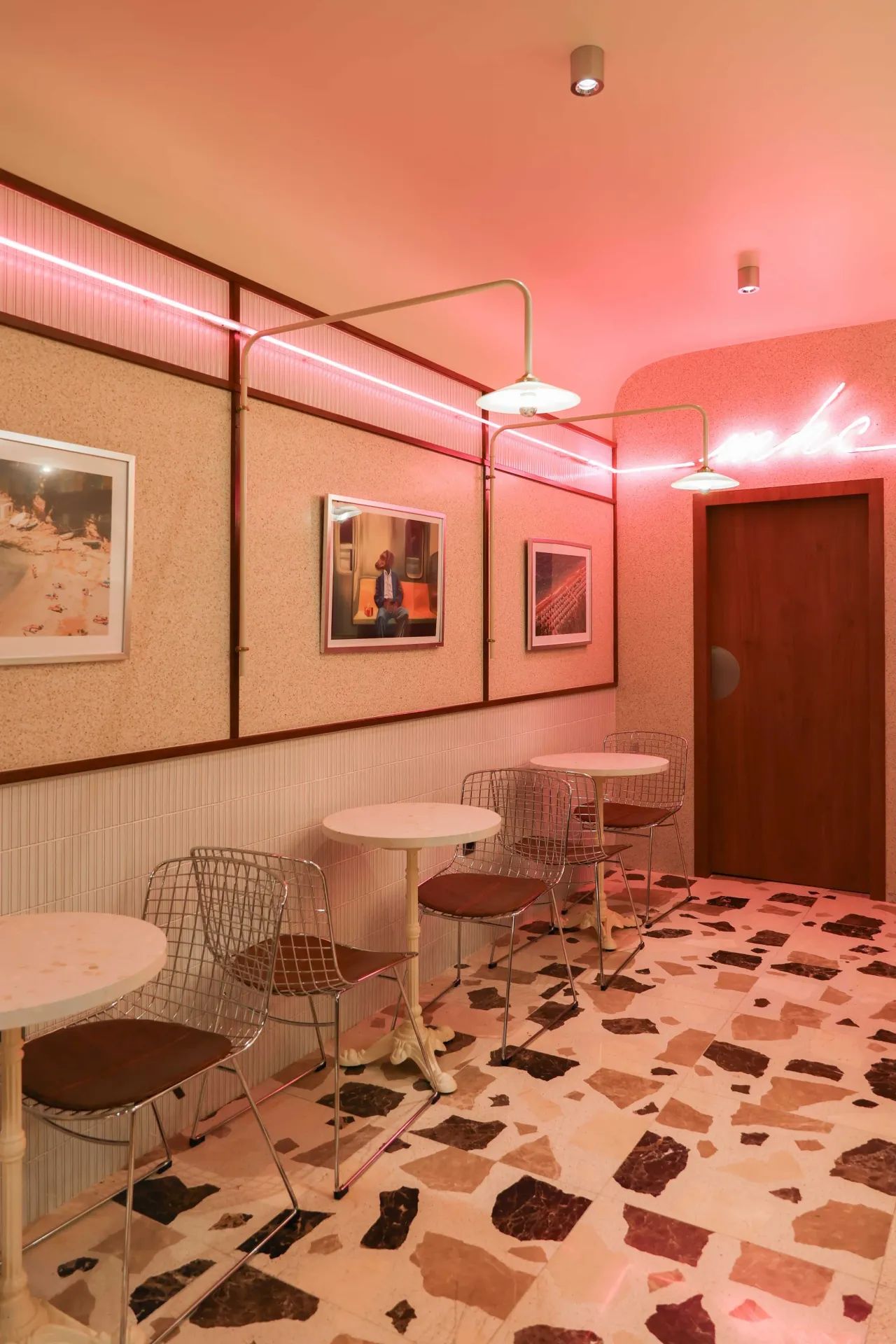 Le mur rose, ses cadres et le néon, au-dessus des tables en terrazzo