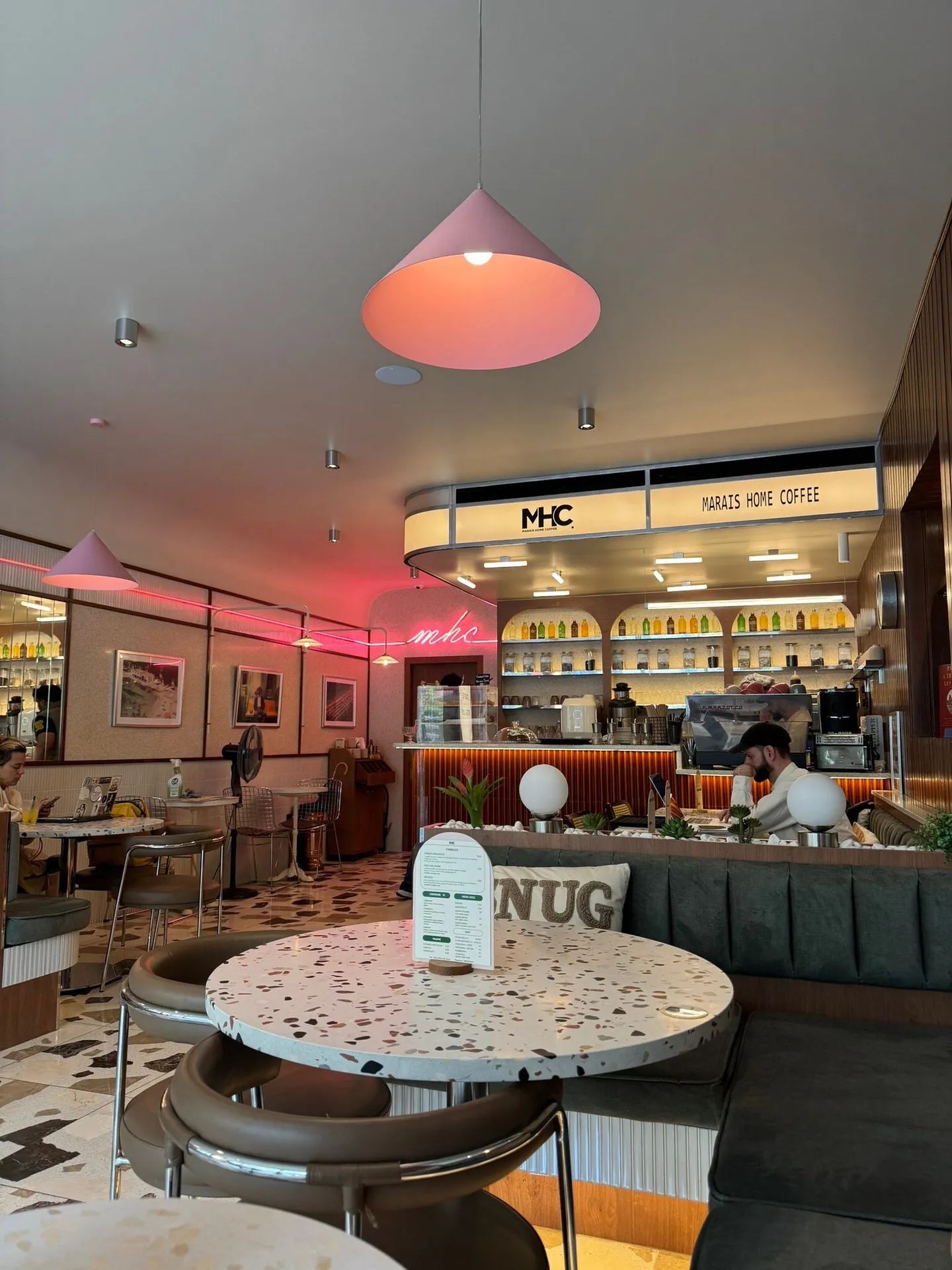 La banquette sauge sous une suspension conique rose, face au comptoir